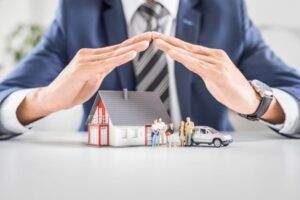Man holding his hands over toy car, family, and house - home and auto insurance bundle